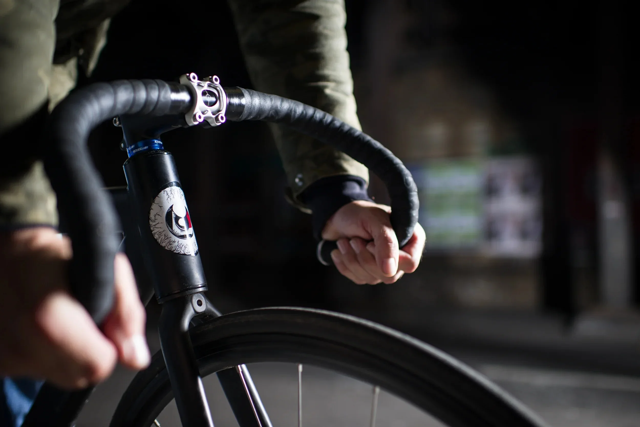Close-up of hands on drop handlebars with a distinctive eye graphic on the bike frame.
